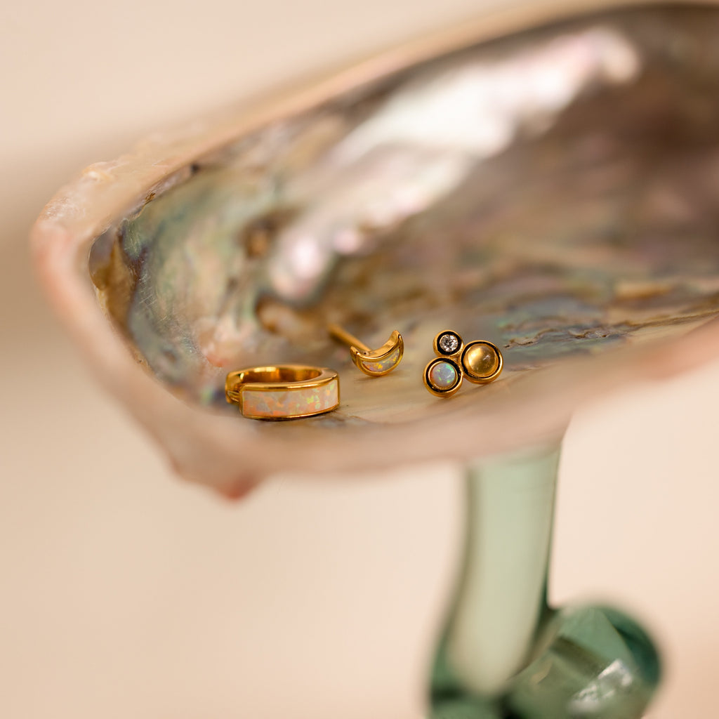 The Opal Inlay Earrings Set is displayed inside an iridescent shell on a glass stand—an elegant gold jewelry gift for her.
