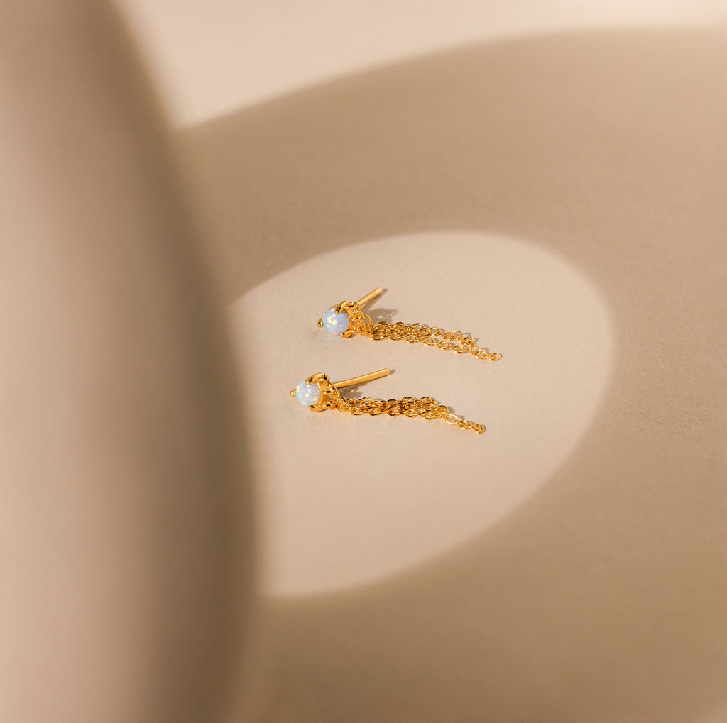 Opal Chain Earrings are displayed on a beige surface in soft, natural light, beautifully highlighting their delicate design and elegance.
