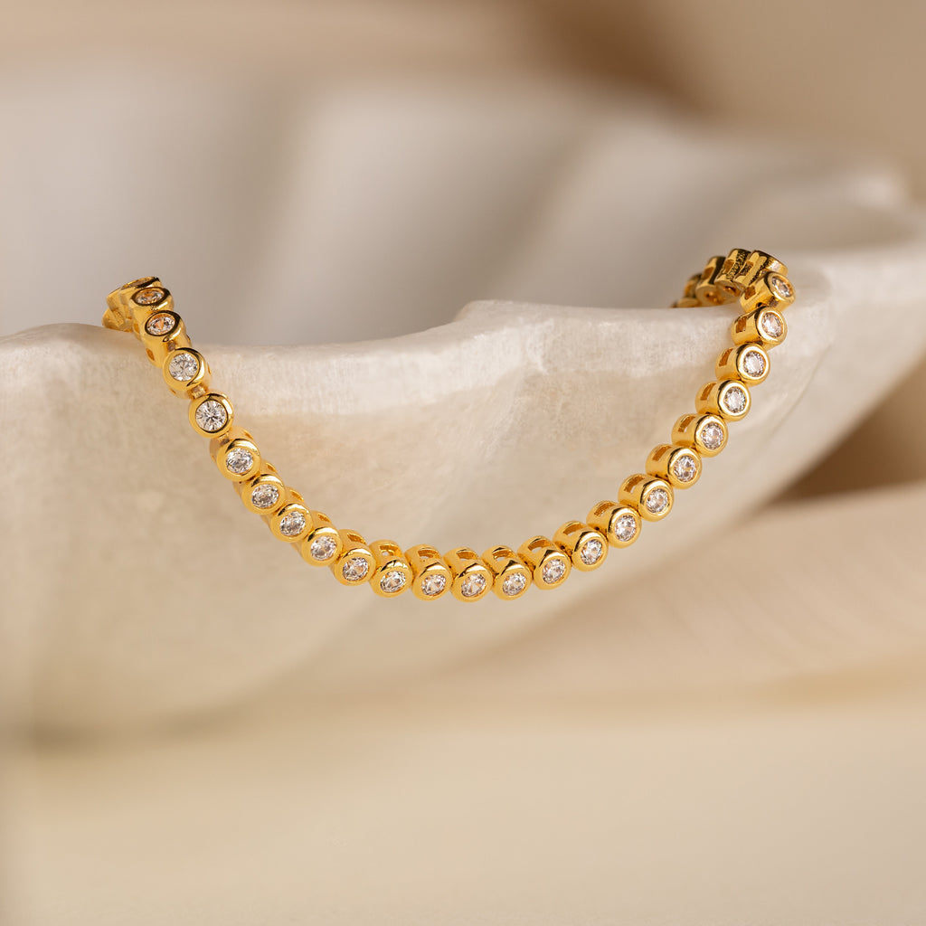 Diamond Bezel Tennis Bracelet displayed on a white, textured surface with a soft beige background—an elegant minimalist bracelet, perfect as a personalized bridal gift.