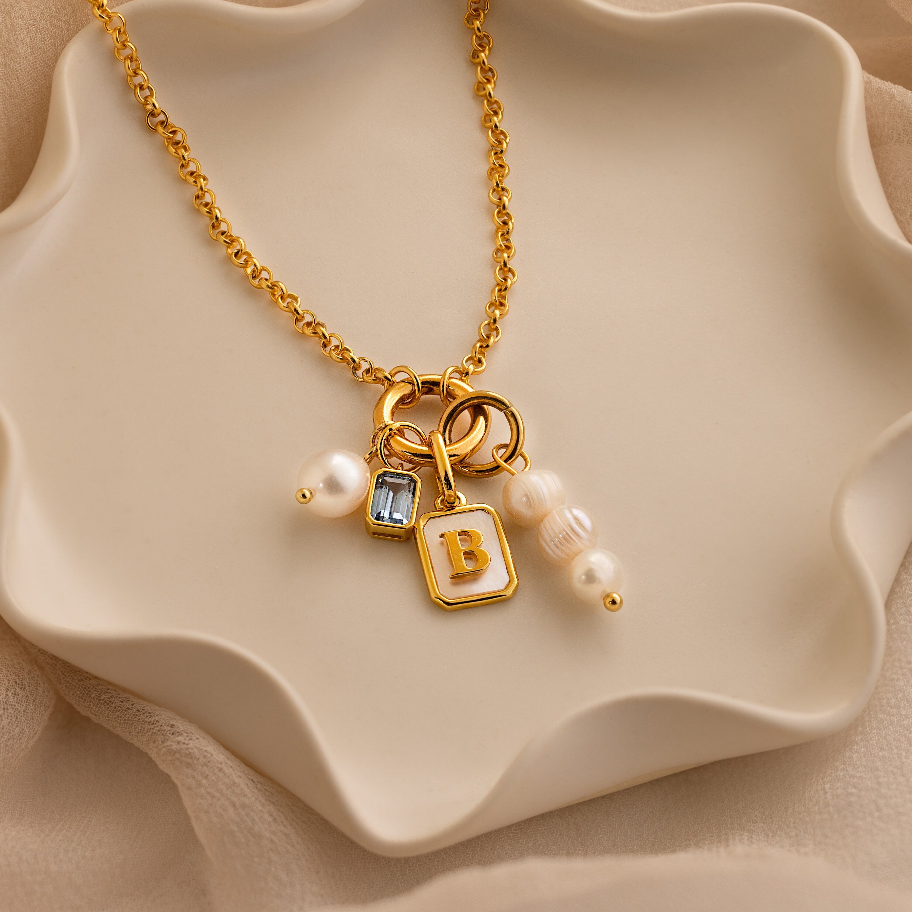 Gold rolo circle clasp necklace with a mother of pearl initial B charm, aquamarine emerald charm, round pearl charm and triple pearl charm
