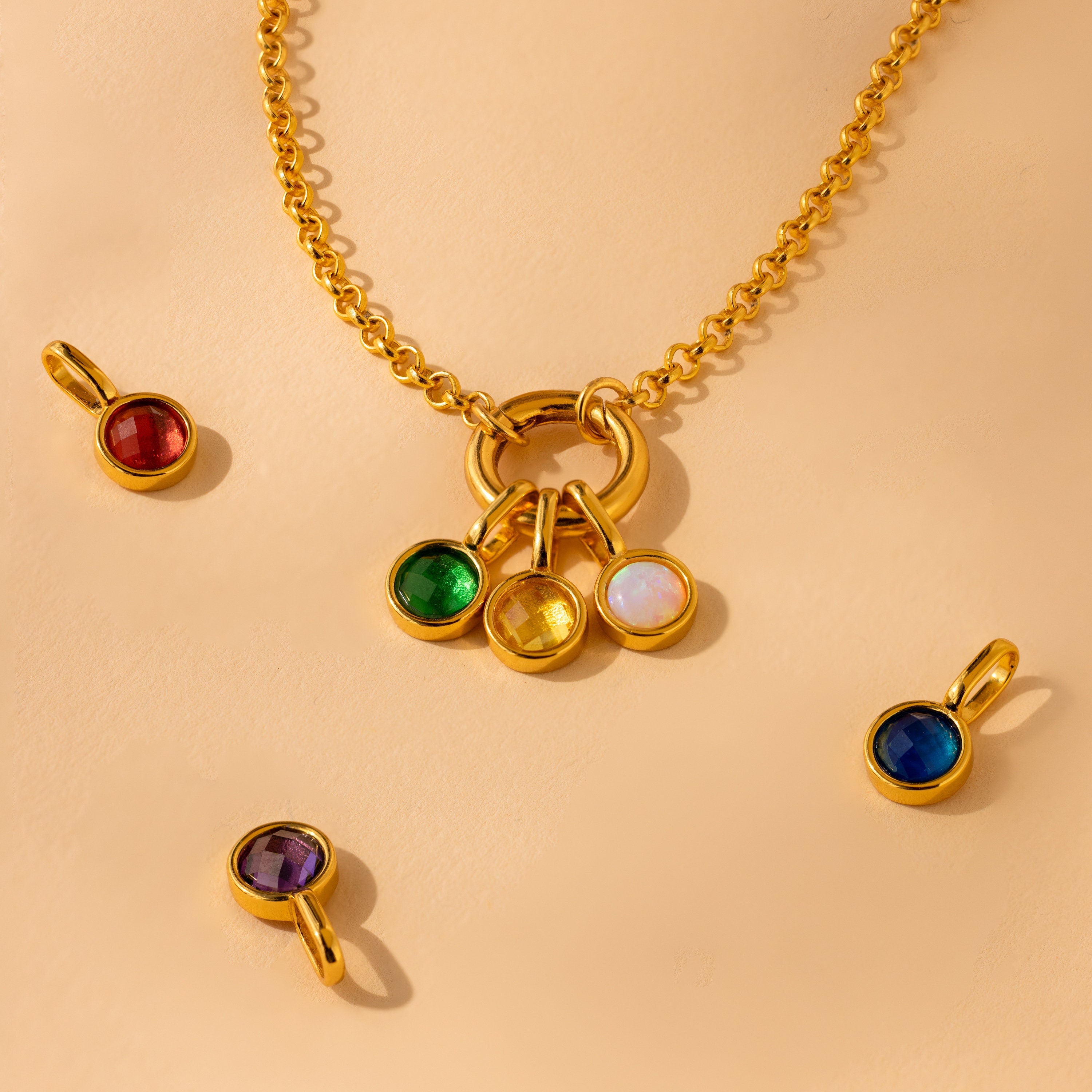 Emerald, Topaz and Opal signet birthstone charms attached to a gold rolo charm necklace. Other signet birthstone charms arranged next to the necklace