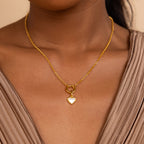 A woman wears the Mother of Pearl Heart Charm necklace, paired with a taupe v-neck top.