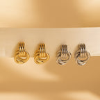Four Triple Knot Earrings—two gold and two silver—displayed along a cream-colored ribbon.