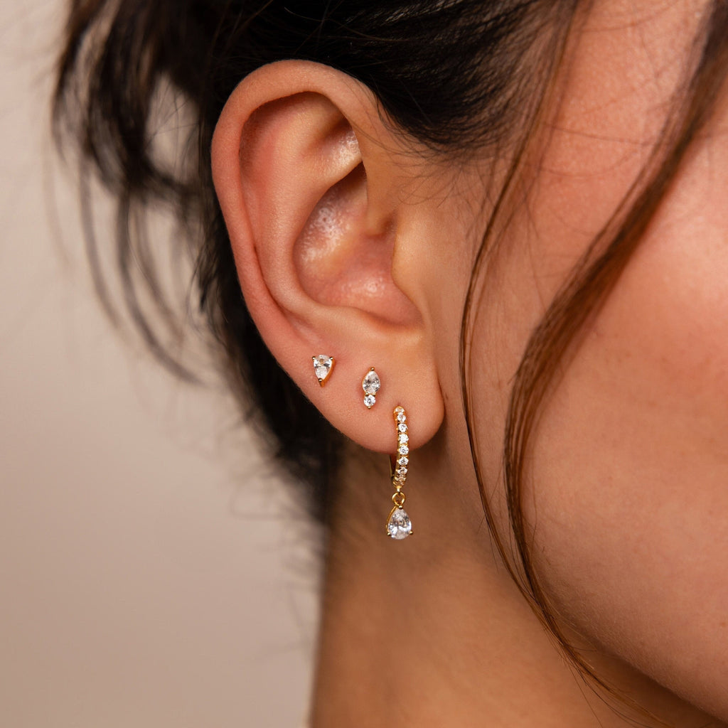 Close-up of a woman's ear wearing the Diamond Drop Earrings Set, featuring three diamond studs and one gold teardrop-shaped diamond drop earring.