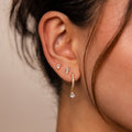 Close-up of a woman's ear wearing the Diamond Drop Earrings Set, featuring three diamond studs and one gold teardrop-shaped diamond drop earring.