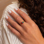 A hand with white nails wears the Toi et Moi Birthstone Ring—a gold customizable ring set with green, pink, and clear gemstones—on a white pleated sleeve, making it a perfect unique Christmas gift.