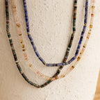 The Rose Quartz Beaded Necklace, featuring colorful beads and gold accents, hangs against a textured white surface—an elegant gift for a best friend.