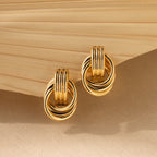 The Triple Knot Earrings, featuring interlocking gold circles, are displayed on a textured neutral background—these elegant earrings make an ideal anniversary gift.