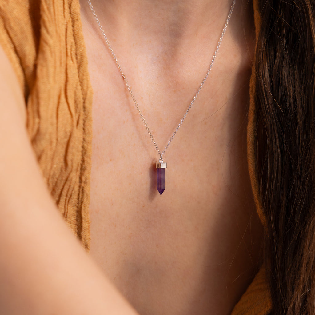 A person wearing the Amethyst Quartz Necklace, featuring a silver chain and crystal charm pendant, shown close up against their chest—a special gift for jewelry lovers.