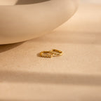 A pair of Opal Link Hoops with small pearls are displayed on a beige surface beside a curved ceramic piece.