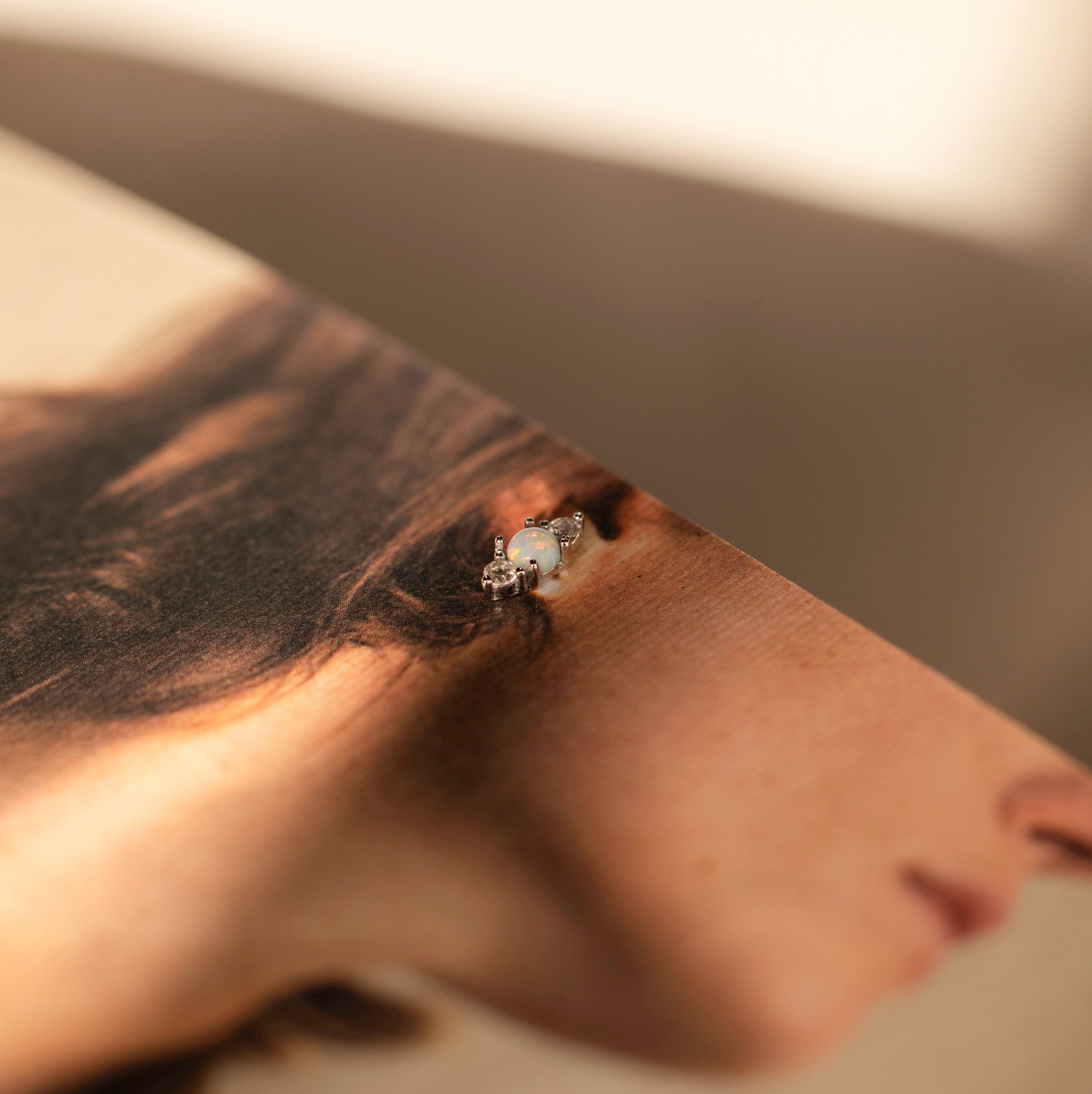 An Opal and Diamond Stud, ideal for cartilage or helix piercings, is displayed on a magazine image featuring a woman's ear and hair.