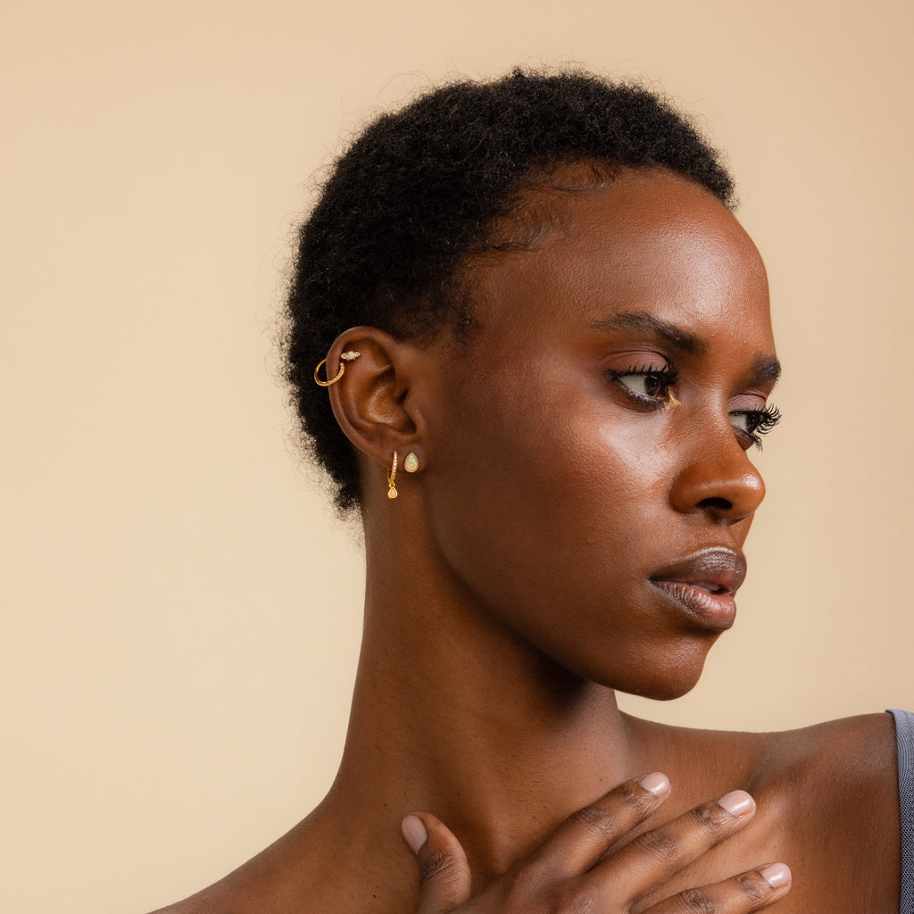 Woman with short curly hair wearing Opal and Diamond Studs, looking to the side with a neutral expression.