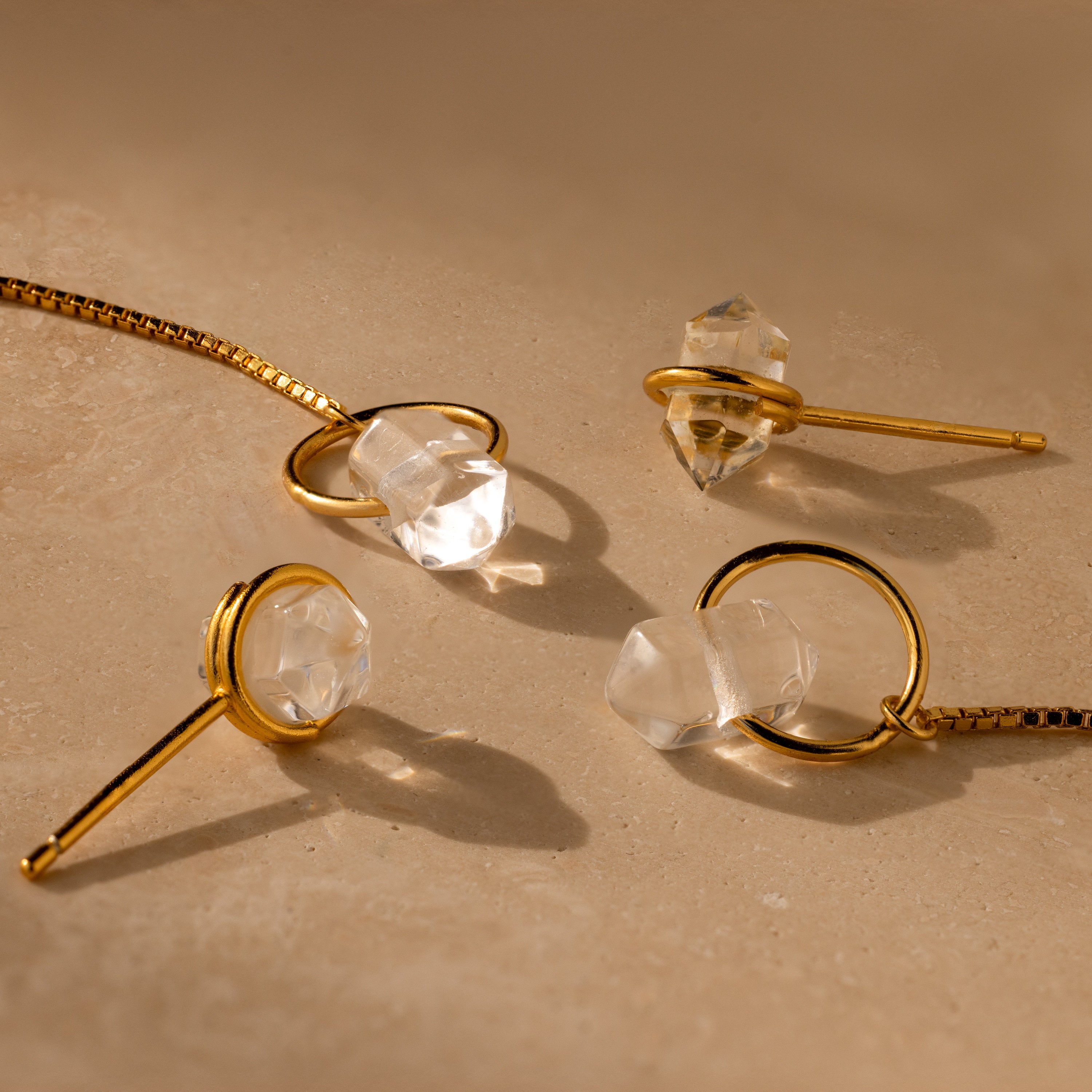 Herkimer Diamond Earrings featuring clear crystal stones rest on a beige surface, illuminated by soft, warm lighting.