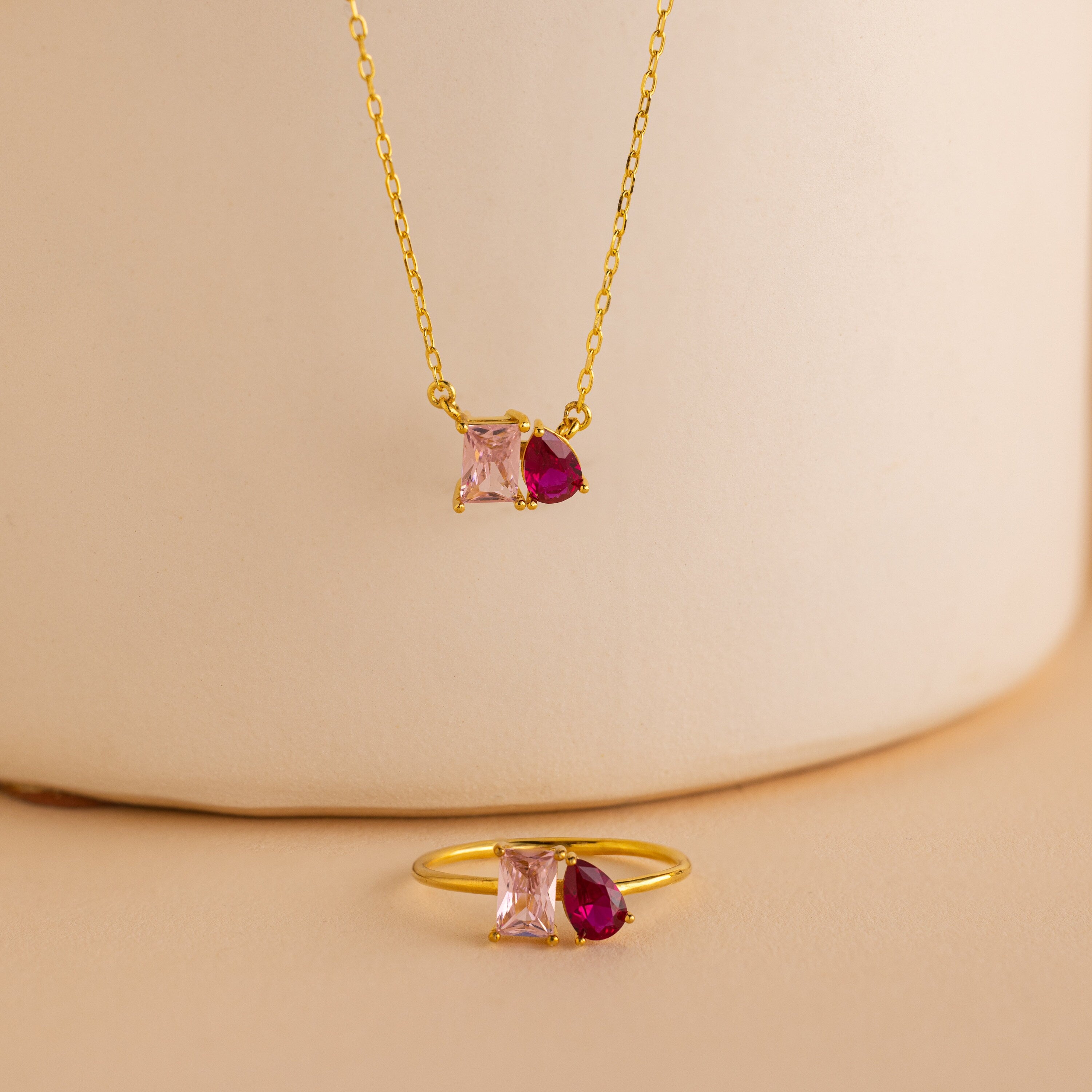 Toi et Moi Birthstone Necklace featuring pink square and red teardrop gemstones on a beige background—ideal for anyone seeking personalized gemstone or custom birthstone jewelry.