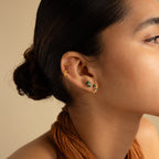 Woman with dark hair in a bun, wearing gold Malachite Inlay Huggies and a brown halter top, shown in side profile to highlight her love for green stone jewelry.