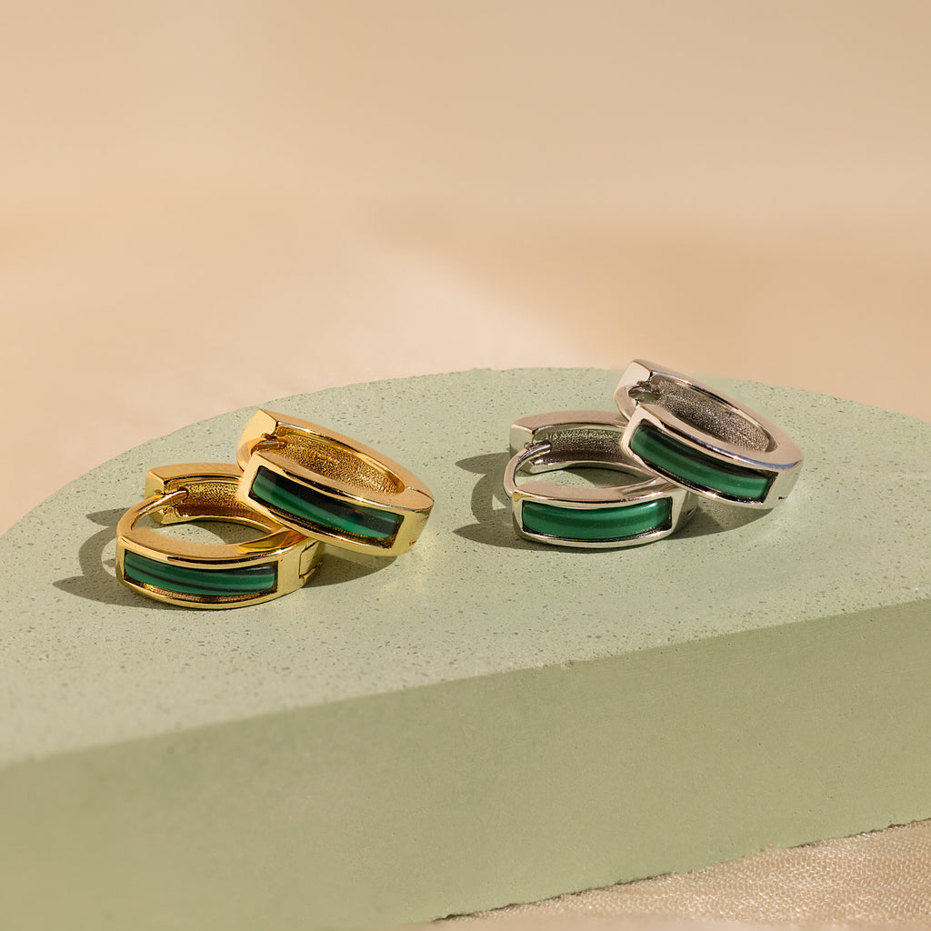 Two pairs of Malachite Inlay Huggies, one gold and one silver, with green rectangular stones, rest on a mint surface—ideal for lovers of green stone jewelry.