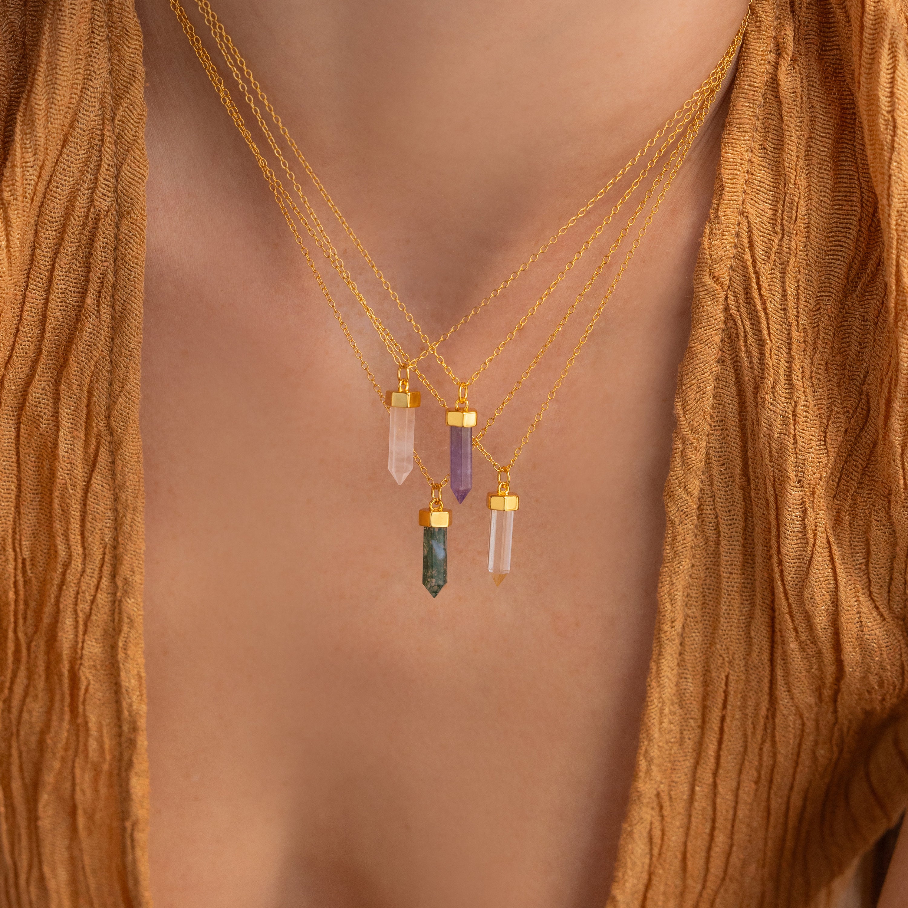 Close-up of three Crystal Quartz Necklaces with hexagonal point pendants, radiating positive energy, worn over a brown textured top.