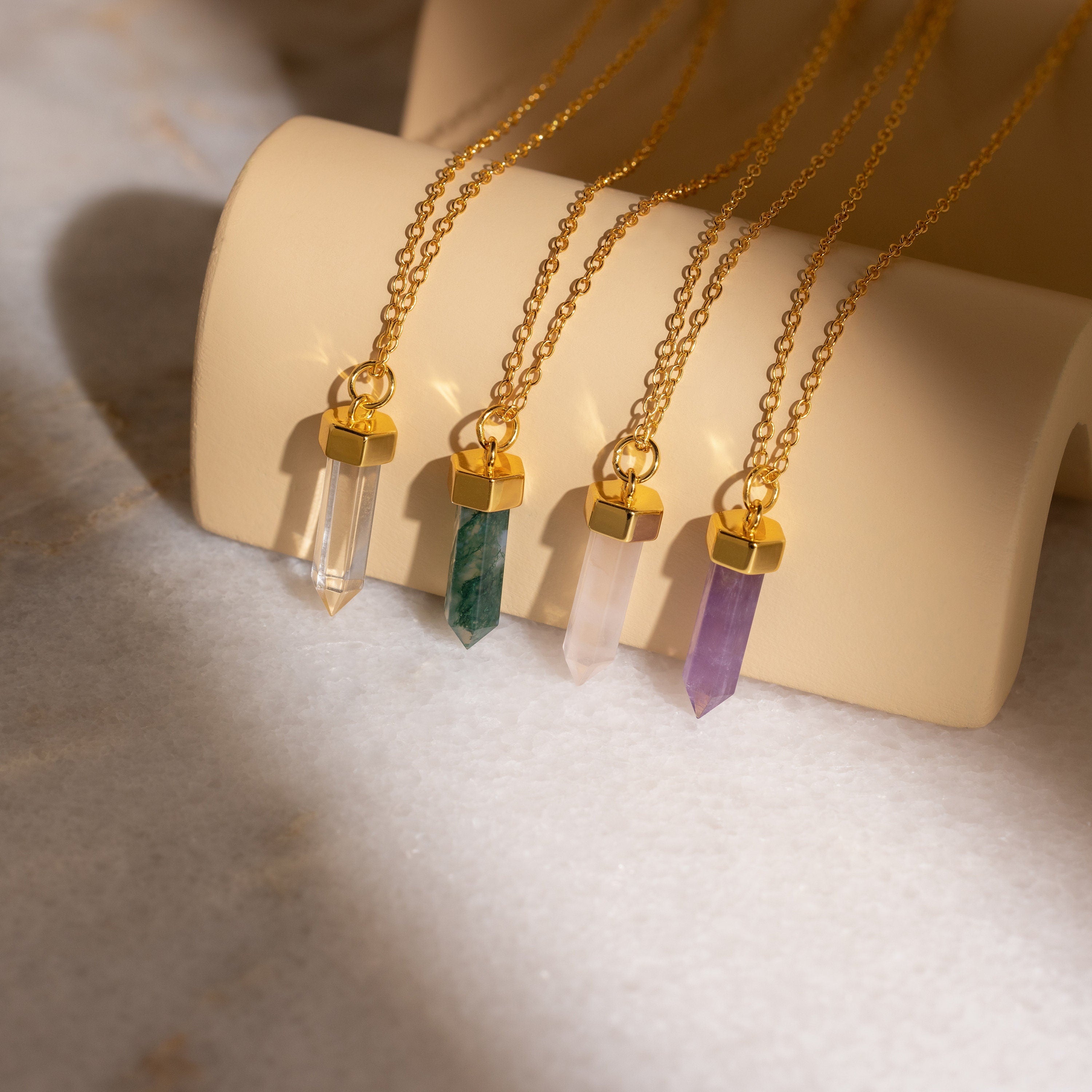 Four Rose Quartz Necklaces—the timeless stone of love—are displayed in different colors on a beige holder.