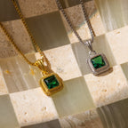 Two Vintage Emerald Pendant Necklaces—one gold, one silver—are displayed on a beige and green checkered surface, perfect for adding an Art Deco touch to your look.