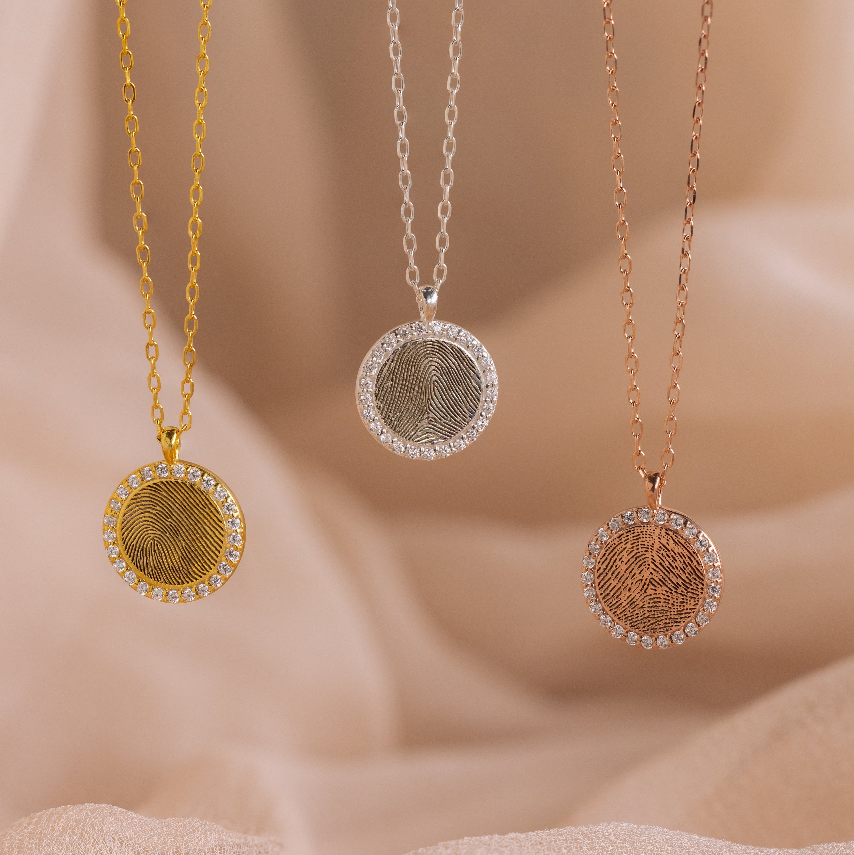 The Pave Fingerprint Coin Necklace is a circular pendant available in gold, silver, and rose gold with a border of gem accents—a personalized engraved memorial gift.