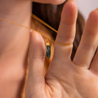 A hand holds a Crystal Quartz Necklaces gold chain with a green hexagonal point pendant, close to the neck.