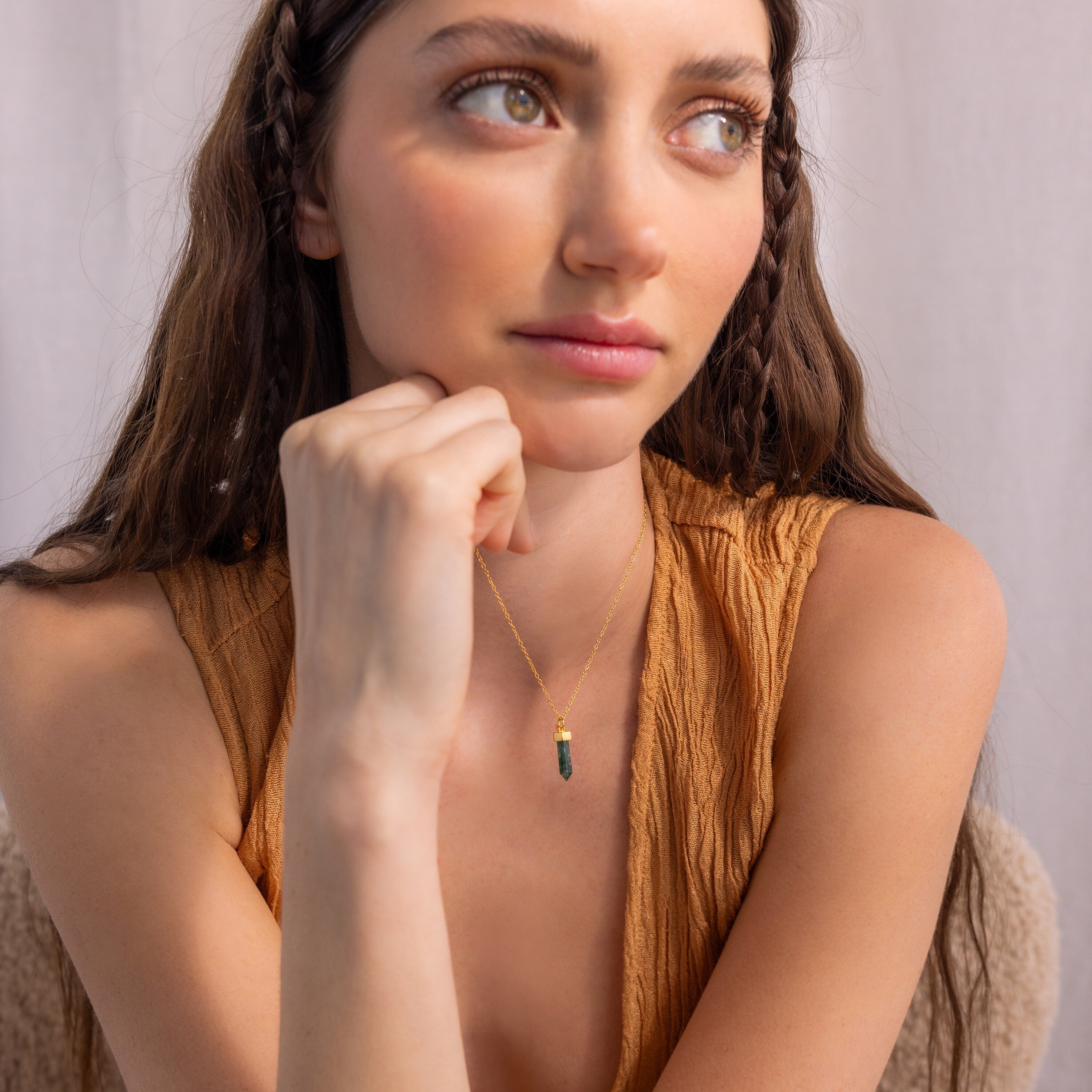 A woman with long brown hair in braids wears a tan top and the Agate Quartz Necklace, gazing thoughtfully to the side.