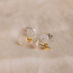 Two pairs of Freshwater Pearl Studs, featuring both gold and silver backs, are displayed on soft beige fabric, showcasing their timeless elegance.