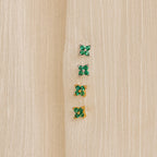Four pairs of small green gemstone earrings—two silver and two gold—are displayed on beige fabric. The nature-inspired Emerald Ivy Flower Studs add a touch of elegance to any look.
