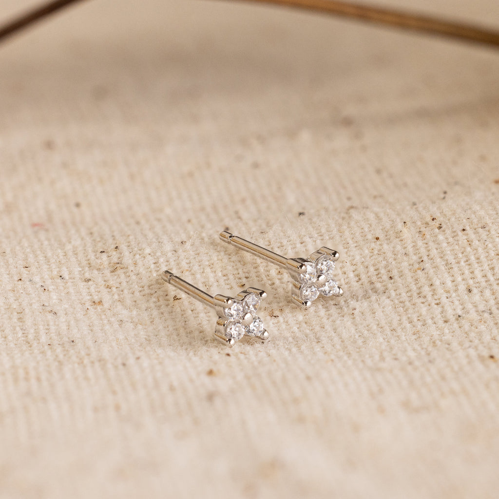 Diamond Ivy Flower Studs feature silver star-shaped designs with small diamonds, presented on a textured beige fabric. Perfect for weddings or adding everyday sparkle, these earrings are a versatile and elegant accessory.