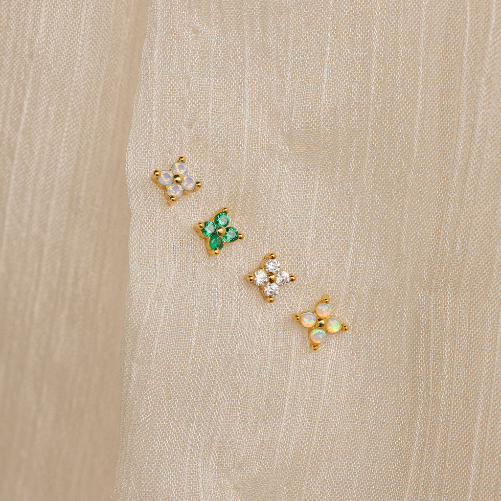 Diamond Ivy Flower Studs—small, gold floral earrings with colorful stones—are displayed on beige fabric and make a versatile accessory, perfect as wedding earrings or for any special occasion.