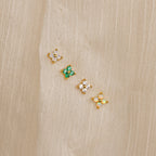 Diamond Ivy Flower Studs—small, gold floral earrings with colorful stones—are displayed on beige fabric and make a versatile accessory, perfect as wedding earrings or for any special occasion.