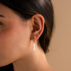 Close-up of a woman's ear wearing three studs and Baroque Pearl Pave Huggies, featuring dazzling pavé details and a long, dangling Baroque pearl.