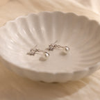 A pair of Diamond Pearl Ear Jackets rests on a white, scalloped dish—perfect for minimalist jewelry lovers.