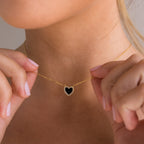 A woman holds the Pave Onyx Heart Necklace close to her neck, its black heart-shaped charm outlined with sparkling crystals.