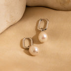 Freshwater Pearl Drop Hoops with elegant pearl drops are shown on a beige fabric background with stone accents, highlighting timeless style.