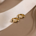The Pearl & Onyx Huggies, featuring delicate pearl and black stone accents, rest on a beige surface beside a white ribbon.