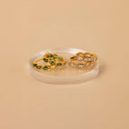 The Emerald Marquise Inlay Huggies, featuring delicate green stones set in gold, are displayed on a round clear stand—perfect dainty earrings to complement your look.