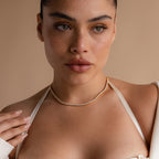 A woman with natural makeup wears the 3 Prong Tennis Necklace in gold and diamonds, paired with a beige top and nude manicure, against a tan background.