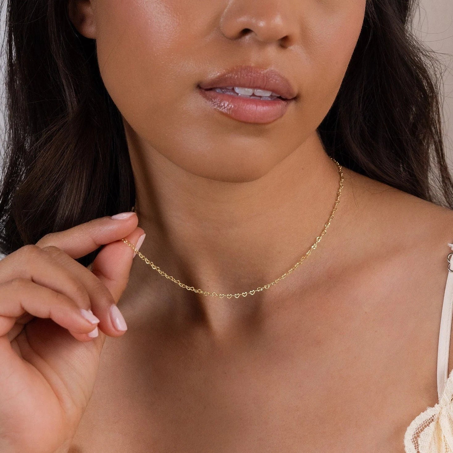 A woman holds her Heart Link Chain Necklace with her right hand, showcasing a close-up of her neck adorned with the romantic interlocking hearts design.