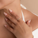 A hand with manicured nails wears the Pave Pearl Stacking Ring Set, featuring gold bands and delicate gemstones, on the ring finger.