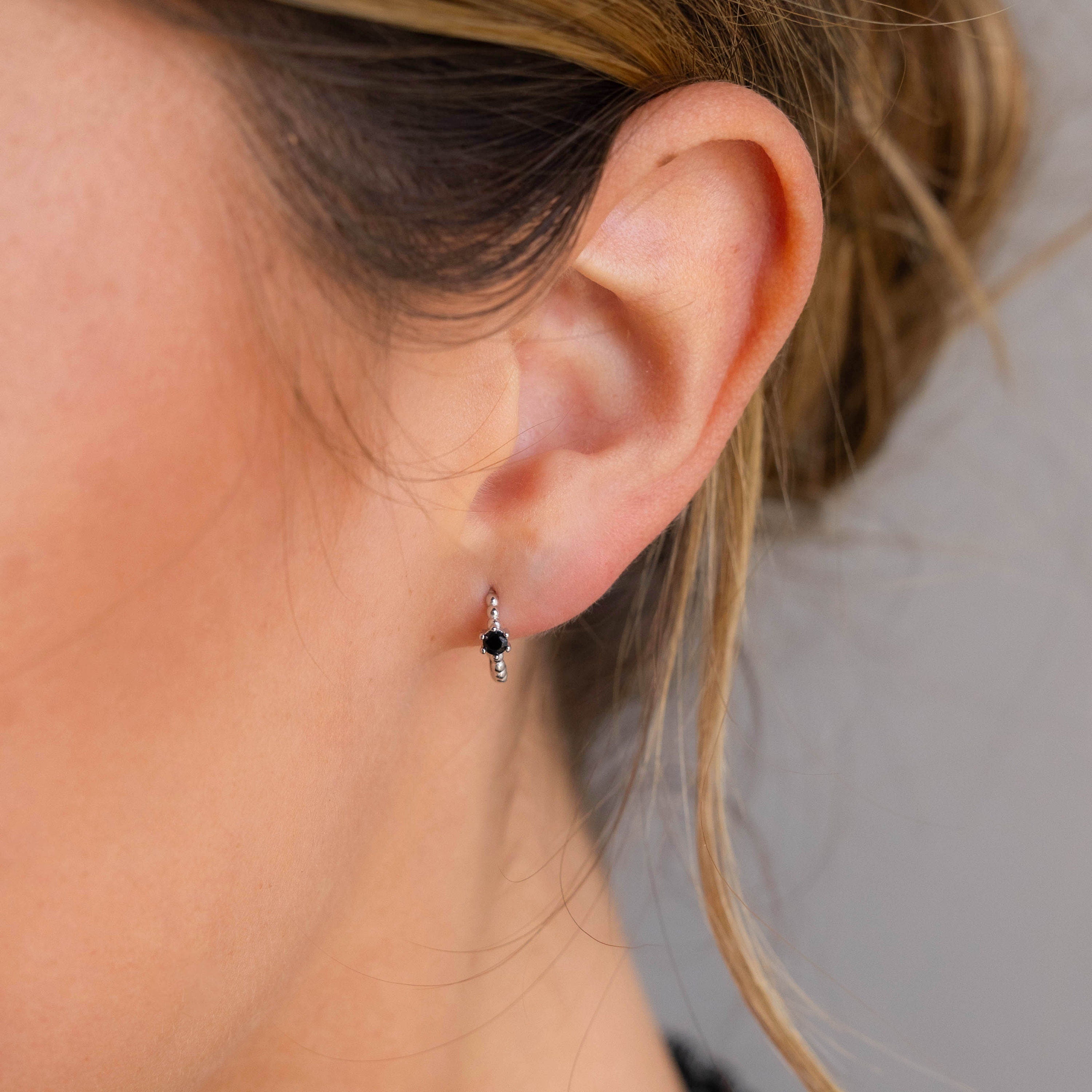 Close-up of a woman's ear wearing Onyx Beaded Huggies—small silver earrings with black onyx beads and dangling silver accents.
