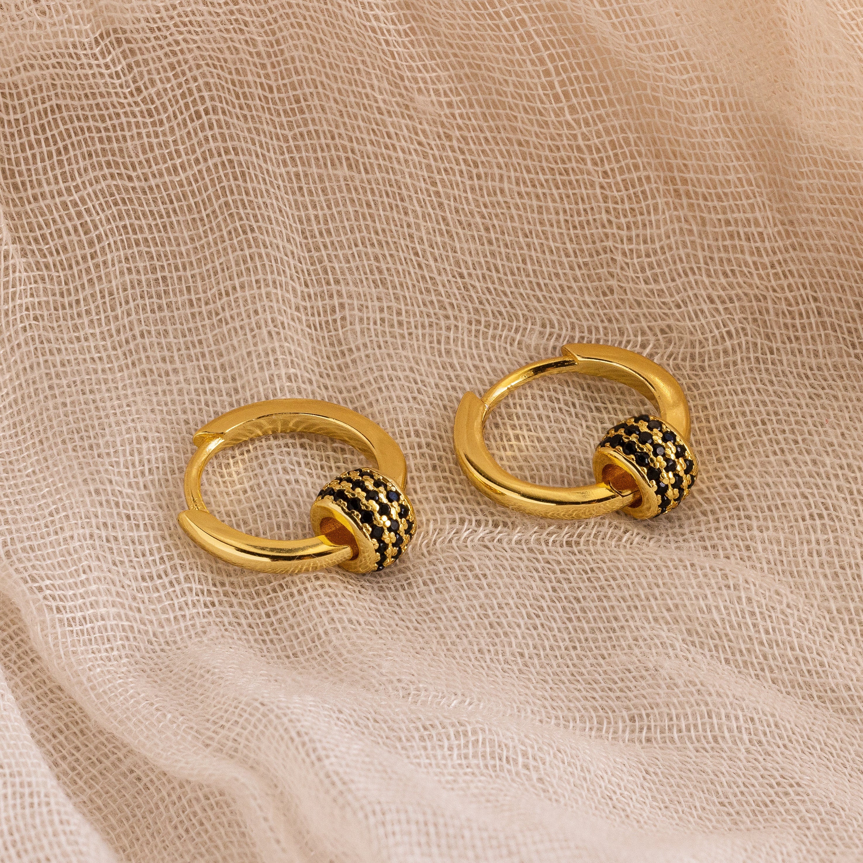 Onyx Pave Beaded Hoops—gold huggie earrings with black beaded accents reminiscent of black onyx pavé—displayed on a light, textured fabric background.