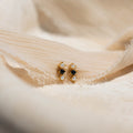 Tiny Onyx Pearl Bar Studs, featuring black stones and small pearls, are elegantly displayed on soft beige fabric for a chic look.