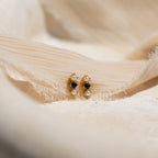 Tiny Onyx Pearl Bar Studs, featuring black stones and small pearls, are elegantly displayed on soft beige fabric for a chic look.