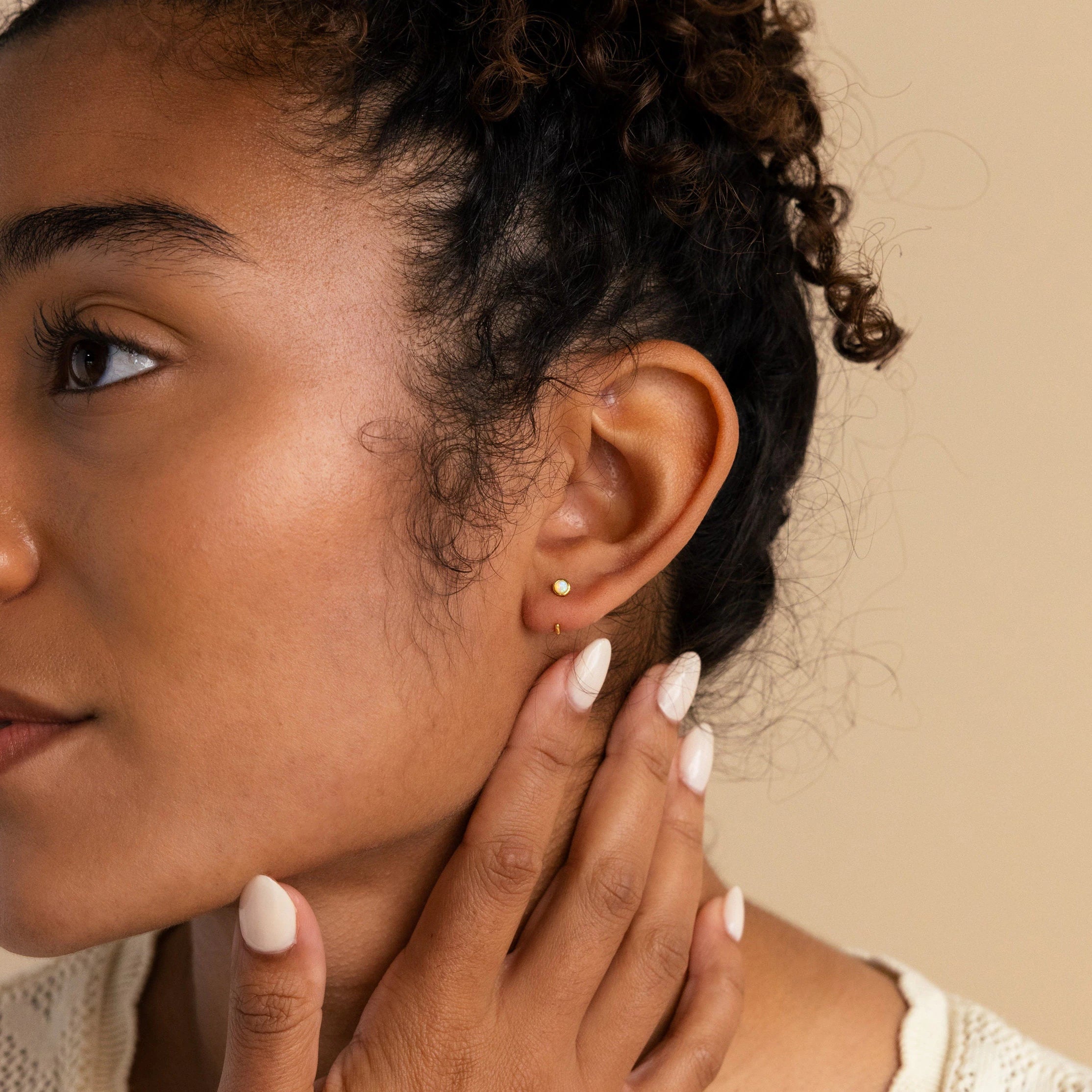 A woman with curly hair touches her neck, showing off manicured nails and her Opal Threader Huggies that perfectly complement her celestial jewelry style.