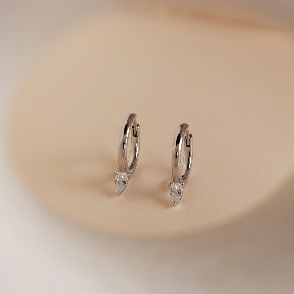 Elegant and timeless, the Pear Diamond Drop Hoops showcase teardrop-shaped crystals on classic silver hoops against a beige background—an ideal wedding accessory.