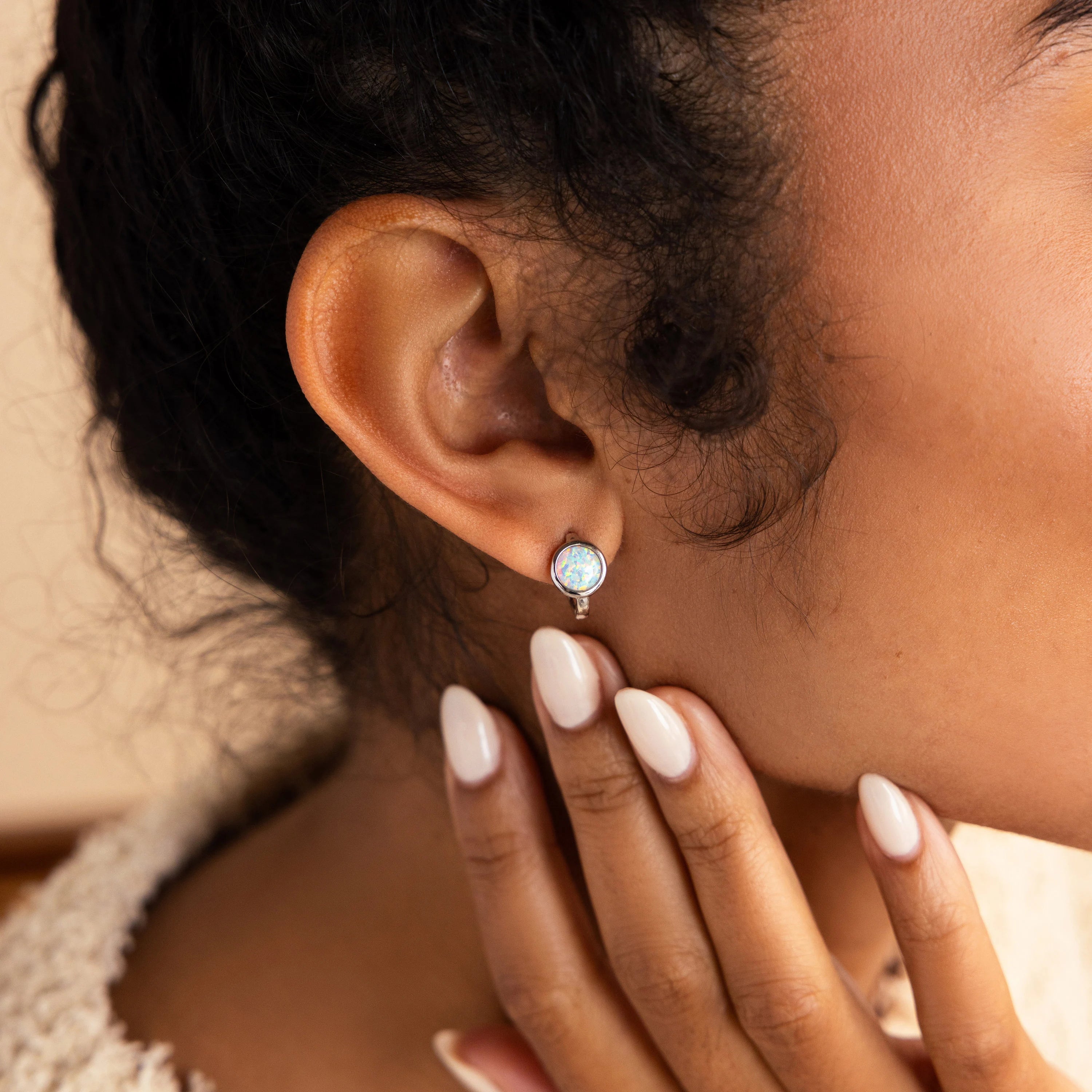 A close-up of a woman's ear wearing Opal Signet Huggies, her manicured nails gently touching her neck, highlighting the elegance of these opal earrings.