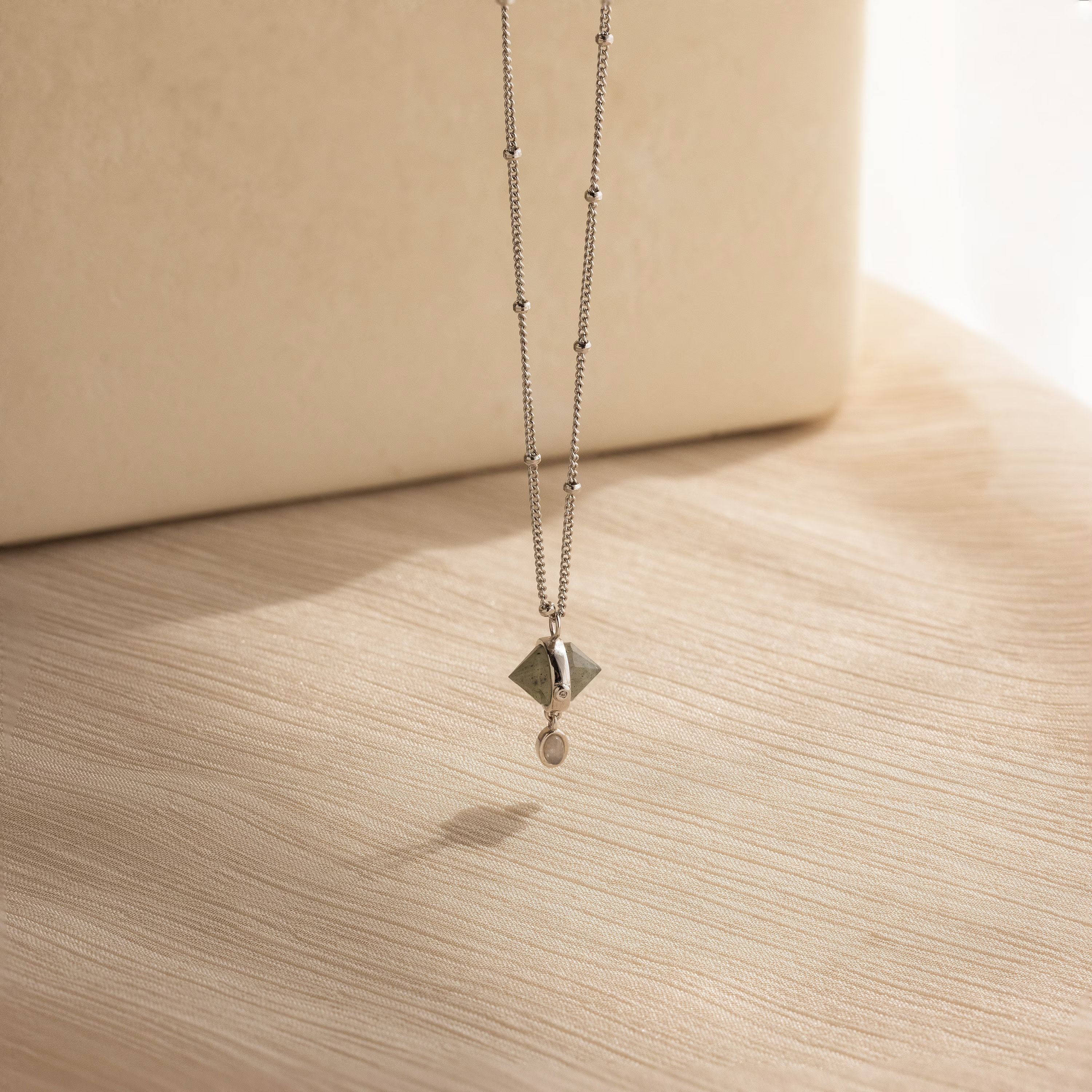 Labradorite & Moonstone Drop Necklace featuring a geometric charm, displayed on light wood with a neutral background.