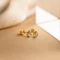The Pear Moonstone Studs, featuring iridescent stones in a gold teardrop design, radiate celestial charm and elegance against a soft beige background.