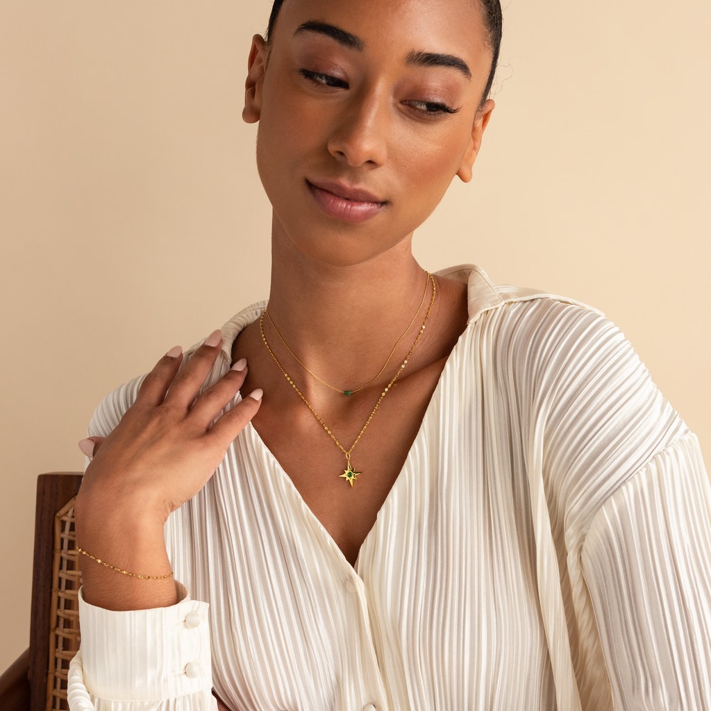 A woman in a white pleated blouse wears the Star Birthstone Necklace, gazing down with a gentle, serene expression.